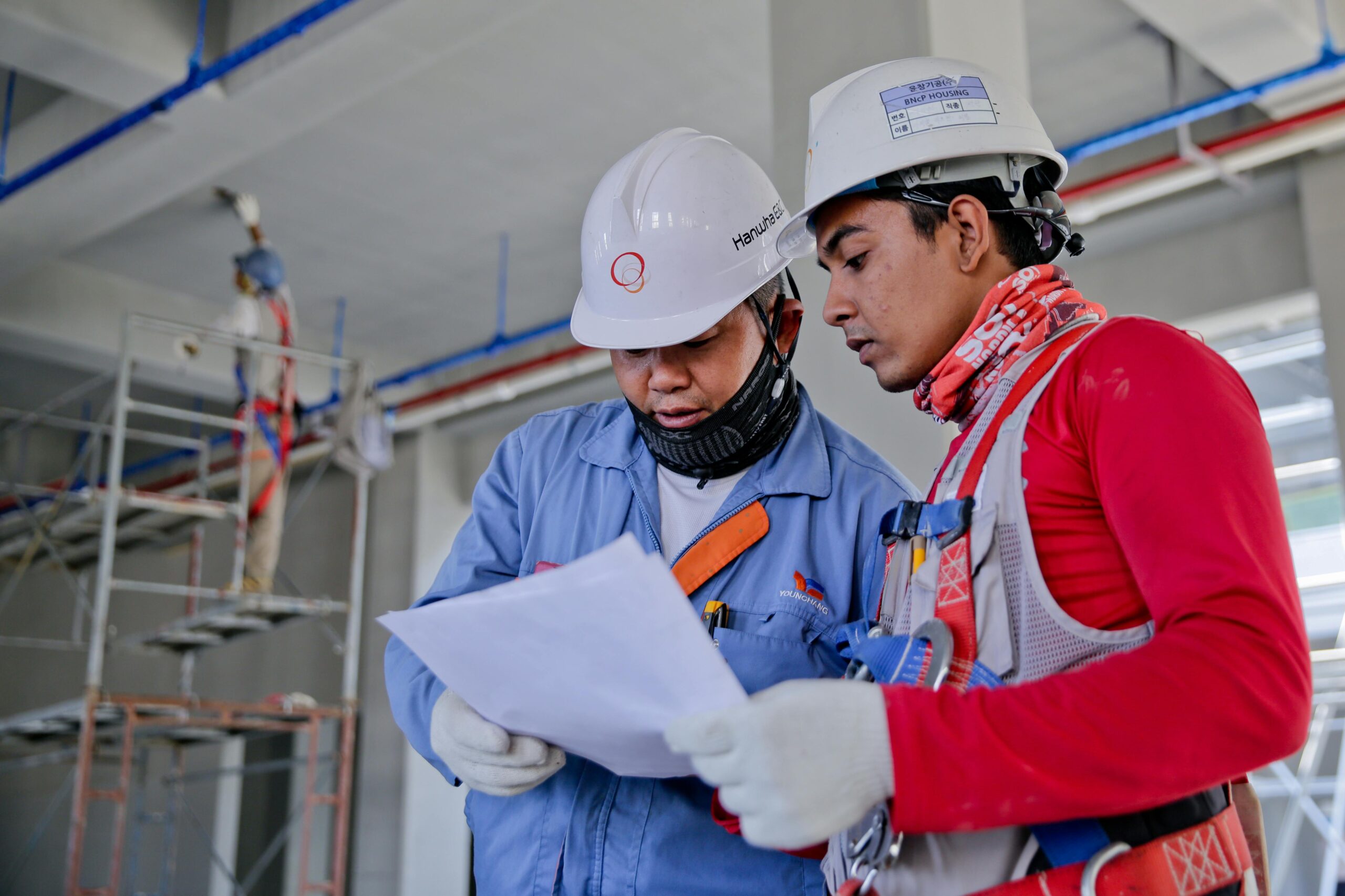 Home - 3 Two engineers in safety helmets reviewing construction plans at a worksite.